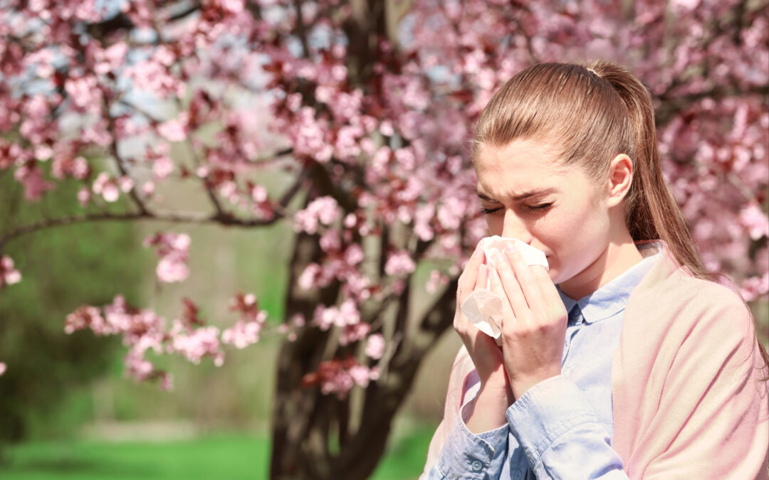 Woman in front of tree sneezing into a tissue.